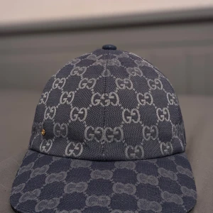 Blå keps från Gucci - Snygg blå keps från Gucci med det ikoniska GG-mönstret i ljusare nyans. Kepsen har en justerbar rem baktill för perfekt passform och är tillverkad i ett slitstarkt material. Ny skick endast allvarliga kunder