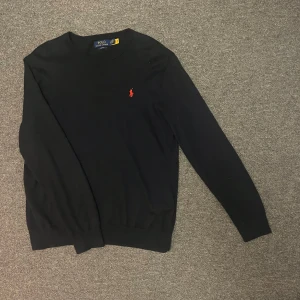 Mörkblå tröja Polo Ralph Lauren - Snygg mörkblå tröja från Polo Ralph Lauren med röd broderad logga på bröstet. Tröjan har en slim fit passform, perfekt för en stilren look. Använd några få gånger. Storlek: L men kan passa M. Inköpt för 1300kr förra året