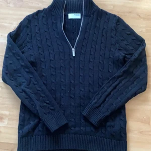 Svart stickad tröja från Selected Homme - Säljer en snygg svart stickad tröja från Selected Homme. Tröjan har en dragkedja framtill och ett klassiskt flätmönster. Perfekt för kyliga dagar med sin höga krage och långa ärmar. Passar både till jeans och chinos. Använd max 3 ggr skick 9/10 inga defekter skitsnygg. 