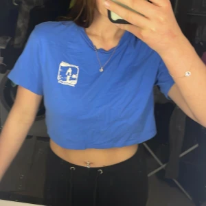 Blå croppad t-shirt - Säljer en blå croppad t-shirt från Divided med tryck 'Surfers Paradise Australia' på bröstet. Perfekt för en avslappnad stil och till sommaren💙🩵🩵