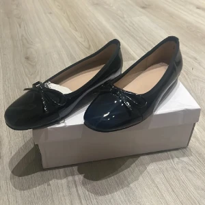 Svarta ballerinaskor med rosett - Snygga svarta ballerinaskor i lack med en söt rosett på tån. Perfekta för en stilren look och bekväma att bära hela dagen. 