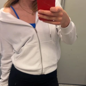 Vit hoodie med dragkedja - Säljer en stilren vit hoodie med dragkedja framtill. Den har en avslappnad passform och är perfekt för en casual look. Huvan har dragsko och tröjan har långa ärmar. Perfekt för kyliga dagar eller som ett lagerplagg.