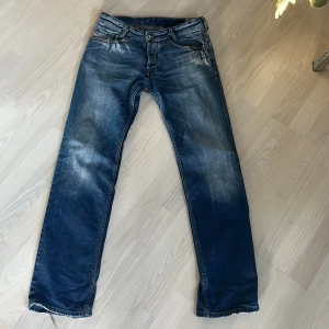 Blå jeansbyxor med detaljer från diesel - Snygga blå jeans med en straight passform och coola slitningar. Byxorna har knappar och dragkedja framtill samt unika detaljer på bakfickorna. Perfekta för en avslappnad stil.
