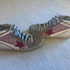 Sneakers med stjärndetalj - Snygga sneakers med en röd stjärna på sidan och silverfärgade snören. Skorna har en kombination av beige och vit färg med en unik design. Perfekta för en trendig look. Säljer pågrund av flytt och för mycket kläder 😊😊