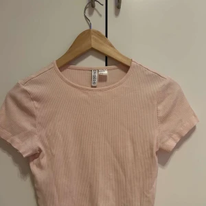 Rosa ribbad t-shirt  - Säljer en söt rosa ribbad t-shirt. Den har en rund halsringning och korta ärmar, perfekt för en avslappnad stil. Passar bra till jeans eller kjol för en enkel look.