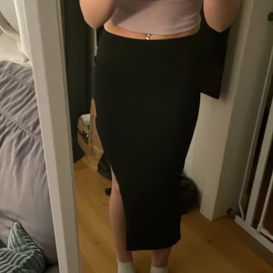 Svart långkjol med slits - Snygg svart långkjol med hög midja och en stilren slits på sidan. Kjolen har en tight passform och är perfekt för en snygg look. Jättefint skick, använd ca 2 ggr✨✨✨Hör av dig vid intresse eller ifall du vill ha fler bilder☺️