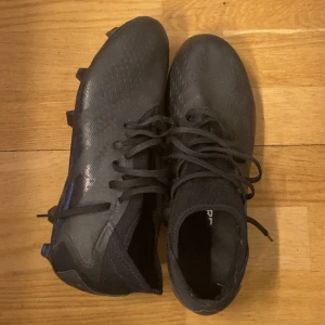 Svarta fotbollsskor med dobbar addidas  - Säljer ett par svarta fotbollsskor med snörning och dobbar för bra grepp på planen. Skorna har en stilren design och är perfekta för fotbollsträning och matcher. Använts ett fåtal gånger och är i mycket bra skick. Pris går att diskutera 