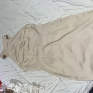  klänning från NA-KD - Snygg beige klänning från NA-KD med halterneck-design. Perfekt för en stilren look. Klänningen har en elegant passform och är tillverkad i ett mjukt material.
