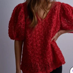 Röd topp - Säljer denna röda fina topp perfekt till jul. Den är i mycket fint skick endast använd vid två tillfällen. Det är som små rosor på hela tröjan verkligen så fint. Från Nelly i storlek M men passar S bra också