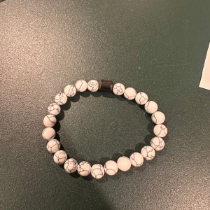 Vitt armband med marmorerade pärlor - Snyggt armband med vita marmorerade pärlor och ett stilrent magnetlås. Perfekt accessoar för att ge din outfit en elegant touch.