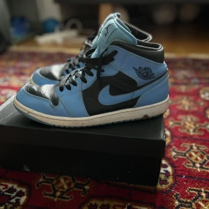 Nike Air Jordans  - Säljer ett par Nike Air Jordans i blått och svart. Skorna har en klassisk design med snörning och en hög siluett. Perfekta för sneaker-entusiaster som vill ha en stilren look.