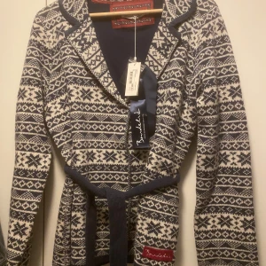 Mönstrad kappa från Bondelid - Snygg mönstrad kappa från Bondelid i blått och vitt. Kappan har ett bälte i midjan och långa ärmar. Perfekt för kyligare dagar med sitt stilrena mönster.