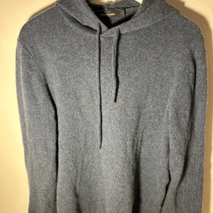 Blå stickad hoodie från Dressman - Mysig grå stickad hoodie från Dressman. Perfekt för kyliga dagar med sin mjuka och bekväma passform. Den har en klassisk huva med dragsko och långa ärmar.