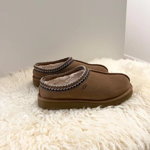 UGG tazz tasman tofflor - Säljer ett par bruna UGG Tasman och mörkbrun detalj som använts endast vid 1-2 tillfällen. Därav är de i nyskick, vilket även syns på sulan. Tycker de är väldigt snygga men kommer tyvärr inte till användning. Väldigt bekväma och praktiska för att göra snabba ärenden samt snygga att ha i vardagen. Funkar både inomhus och utomhus. Storlek 39 men passar perfekt för mig som har storlek 38.