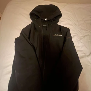 Svart jacka från Peak Performance - Säljer en svart jacka från Peak Performance med huva och dragkedja. Perfekt för kyliga dagar med sin stilrena design och praktiska fickor.