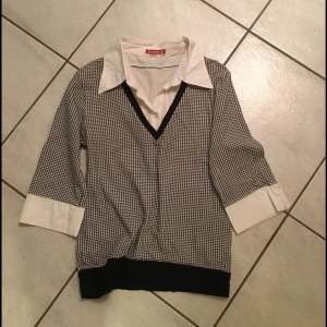 Svartvit rutig tröja från Benetton - Snygg svartvit rutig tröja från Benetton med v-ringning och trekvartsärmar. Tröjan har en vit krage och vita manschetter som ger en stilren look. Perfekt för en chic vardagsstil.