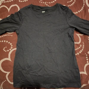 Mörkgrå långärmad topp från H&M - Säljer en enkel och stilren mörkgrå långärmad topp från H&M. Perfekt för lager-på-lager eller att bära som den är. Gjord i mjukt material för bekväm passform.