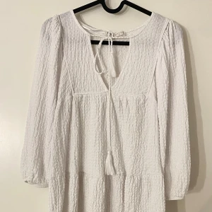 Vit klänning från Pull&Bear - Säljer en vit klänning från Pull&Bear med knytband framtill och en lätt textur. Super söt 