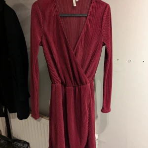 Vinröd omlottklänning Nelly Trend  - Snygg vinröd omlottklänning med ribbad textur och långa ärmar. Klänningen har en v-ringad design.