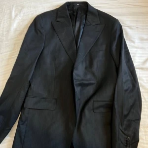 Sir of sweden, Svart randig kostym - Elegant svart kostym med subtila ränder. Kavajen har klassisk design med knappar och fickor. Byxorna matchar perfekt med samma randiga mönster. 