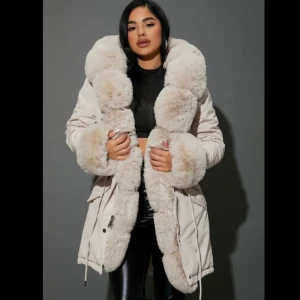 Vit parkajacka med pälsdetaljer - Säljer en elegant vit parkajacka med lyxiga pälsdetaljer längs huva och framkant. Jackan har långa ärmar och stängs med både dragkedja och knappar. Perfekt för kalla vinterdagar. Jackan är ny använt 2 gånger ingår päls till armarna 