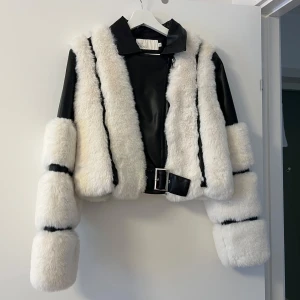 Vit och svart pälsjacka från NLY Trend - Såå snygg vit och svart pälsjacka från NLY Trend med läderdetaljer. Jackan har ett coolt bälte i midjan och dragkedja framtill. Perfekt för att sticka ut i mängden! Aldrig använd och tyvärr för liten på mig. Nypris 1000 kr. Ej prutbar.
