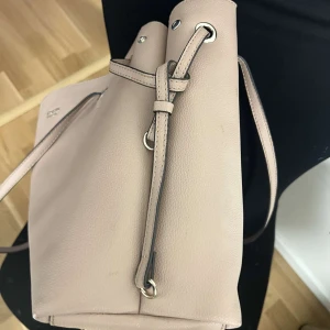 Beige Guess axelväska med dragkedja - Snygg beige axelväska i syntetmaterial med praktisk dragkedja och justerbara axelremmar. Perfekt för att bära med sig alla nödvändigheter. Enkel och stilren design som passar till många tillfällen. Dock har jag tappat bort taggen som syns på sista bilden