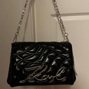Svart quiltad axelväska från Karl Lagerfeld - Snygg svart axelväska i quiltat mönster från Karl Lagerfeld. Väskan har en kedjerem och en stor logotypdetalj framtill. Perfekt för att ge en lyxig touch till outfiten- Utsåld på nästan alla hemsidor Nypris - 3300kr       *öppen för förhandling vid snabb affär 