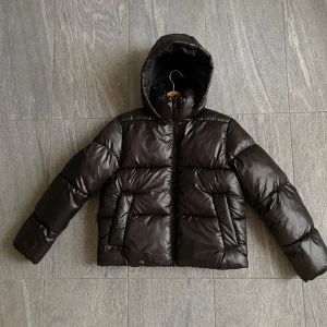 Svart pufferjacka från H&M - Snygg svart pufferjacka från H&M i storlek S. Jackan har en huva och är tillverkad i 100% polyester, perfekt för kyliga dagar. Den har en dragkedja framtill och långa ärmar.                                Den är ny och oanvänd💗