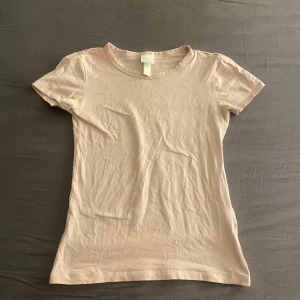 rosa t-shirt från H&M - Säljer en enkel och stilren rosa t-shirt från H&M Basics. Den är kortärmad och tillverkad i ett mjukt material, perfekt för vardagsbruk. Passar bra till jeans eller kjol för en avslappnad look.