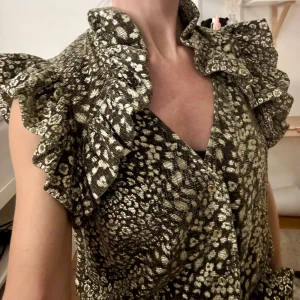 Glittrig jumpsuit från Ida Sjöstedt - Glittrig guldig jumpsuit från Ida Sjöstedt. Knytskärp i midjan. Stor i storleken.