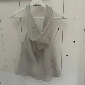 Grå ärmlös topp från Zara - Snygg grå ärmlös topp från Zara med en elegant draperad hals. Perfekt för en stilren look, tillverkad i ett mjukt och bekvämt material.