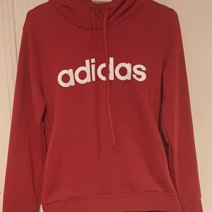 Röd hoodie från Adidas - Säljer en snygg röd hoodie från Adidas med vit logga på framsidan. Skön tröja med bekvämt material.