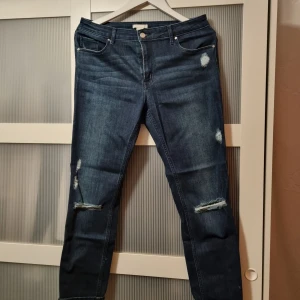 Blå jeans från H&M - Snygga blå jeans från H&M med slitna detaljer på knäna och låren. De har en klassisk femficksdesign och knappgylf. Perfekta för en avslappnad stil.