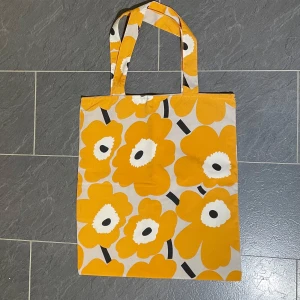 Marimekko shoppingväska i gult, grått och svart, hemmasydd  - Snygg marimekko shoppingväska med Unikko mönster i gult, grått  och svart . Väskan har långa handtag och en praktisk tryckknapp för stängning. Perfekt för en dag på stan eller till jobbet eller skolan funkar också bra som en färgglad accessoar. Hemmasydd i tyg av hög kvalité med noggrannhet och använd vid ett par tillfällen, nyskick. 