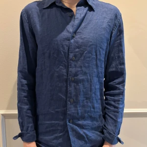 Blå linneskjorta - Tvärsnygg marinblå linneskjorta från Uniqlo. Köpt i somras. Säljs pga av att den har blivit för liten. 100% linne och passar som sagt både till jeans eller ett par sköna shorts. Storlek XS, tveka inte att höra av dig vid minsta fundering. 