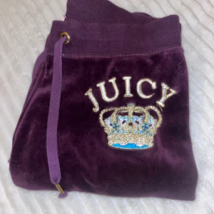 Lila byxor från Juicy Couture  - Säljer ett par lila byxor från Juicy Couture med broderad krona och texten 'JUICY' på framsidan!  De är vintage från 2005. 💜Byxorna är lite korta på mig som är 168. Det står att byxorna är i storlek M men passar mer en person med S. Tryck gärna på köp nu! Om du har frågor är det bara att kontakta. 😁