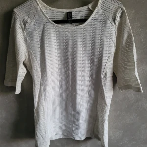 Vit topp med trekvartsärm från Raoul - Snygg vit topp från Raoul med trekvartsärm och ett diskret mönster. Perfekt för en stilren look. Toppen har en rund halsringning och är tillverkad i ett lätt material.