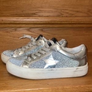 Glittriga sneakers från Steve Madden - Snygga trendiga sneakers från Steve Madden i silver med glittriga detaljer och stjärnmönster på sidorna. Skorna har snörning och en bekväm vit sula. Välanvända men i bra skick, däremot lite defekter (kan skicka bilder) men inget som påverkar funktionen av skor, de allra flesta defekterna är innanför skorna. Tvättas självklart innan de skickas! Osäker på storlek då det ej står, men jag som har 38/39 kan tycka de är lite lite små, men passar lite tajtare, så skulle gissa på 37-38 💗