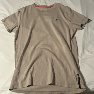 Beige t-shirt från Moose Knuckles - Snygg beige t-shirt från Moose Knuckles med korta ärmar och diskret logga på bröstet. Perfekt för en avslappnad stil.