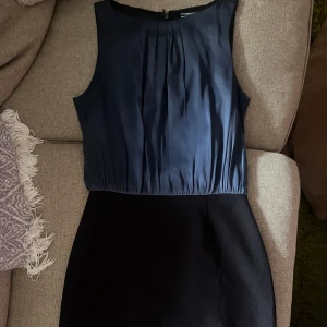 Blå och svart klänning från Tommy Hilfiger - Elegant ärmlös klänning(size 4/S) från Tommy Hilfiger i en stilren kombination av blått och svart. Klänningen har en rund hals och en dragkedja i ryggen för enkel påklädning. Perfekt för en chic och sofistikerad look.