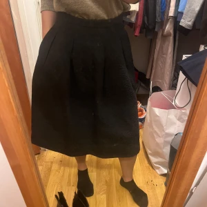 Svart kjol från H&M - Snygg svart kjol från H&M med en elegant textur. Kjolen har en klassisk A-linjeform och knäppning i midjan. Perfekt för en stilren look.