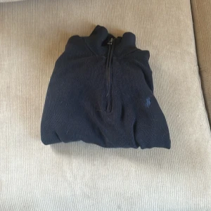 Ralph Lauren Half zip - Säljer en stilren mörkblå tröja från Ralph Lauren med dragkedja och hög krage. Perfekt för kyligare dagar och ger en klassisk look. Tröjan har en diskret logga på bröstet. Sitter perfekt o knappt använd