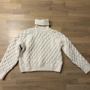 Vit stickad polotröja - Mysig vit stickad polotröja med ett klassiskt flätmönster. Perfekt för kyliga dagar med sin höga krage och långa ärmar. En tidlös garderobsfavorit! Oanvänd (saknar prislapp). 