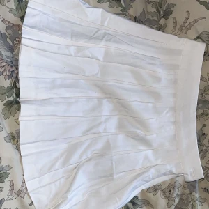 Vit plisserad kjol från FB Sister - Snygg vit plisserad kjol från FB Sister i en kort modell. Kjolen har en knapp och dragkedja i sidan för enkel på- och avtagning. 