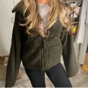 Olivgrön teddyjacka med dragkedja - Mysig olivgrön teddyjacka med dragkedja framtill. Jackan har en avslappnad passform och långa ärmar, perfekt för kyligare dagar. Den fluffiga texturen ger en trendig look. 