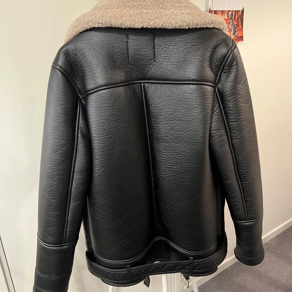 Snygg svart jacka från Stradivarius med beige teddyfoder. Jackan har en asymmetrisk dragkedja och bred krage. Perfekt för kyligare dagar med sin stilrena design och bekväma passform.. Takit.