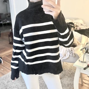 Svart och vit randig polotröja - Säljer en stilren svart och vit randig polotröja med långa ärmar. Perfekt för kyligare dagar med sin mysiga och varma design. Tröjan har en klassisk polokrage och är tillverkad i ett mjukt material.