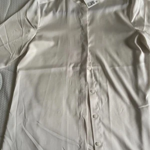Vit blus från H&M - Säljer en stilren vit blus från H&M med knappar framtill. Blusen har långa ärmar och en klassisk krage, perfekt för en elegant look. Materialet är mjukt och bekvämt.