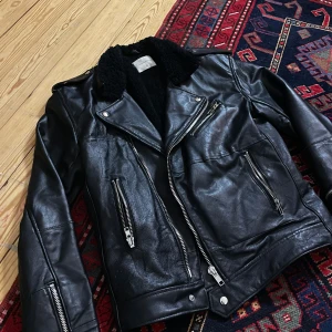 Svart skinnjacka från Deadwood - Snygg svart skinnjacka från Deadwood med dragkedjor och en mjuk, pälsliknande insida. Jackan har en klassisk bikerstil med flera fickor och detaljer i silver. 